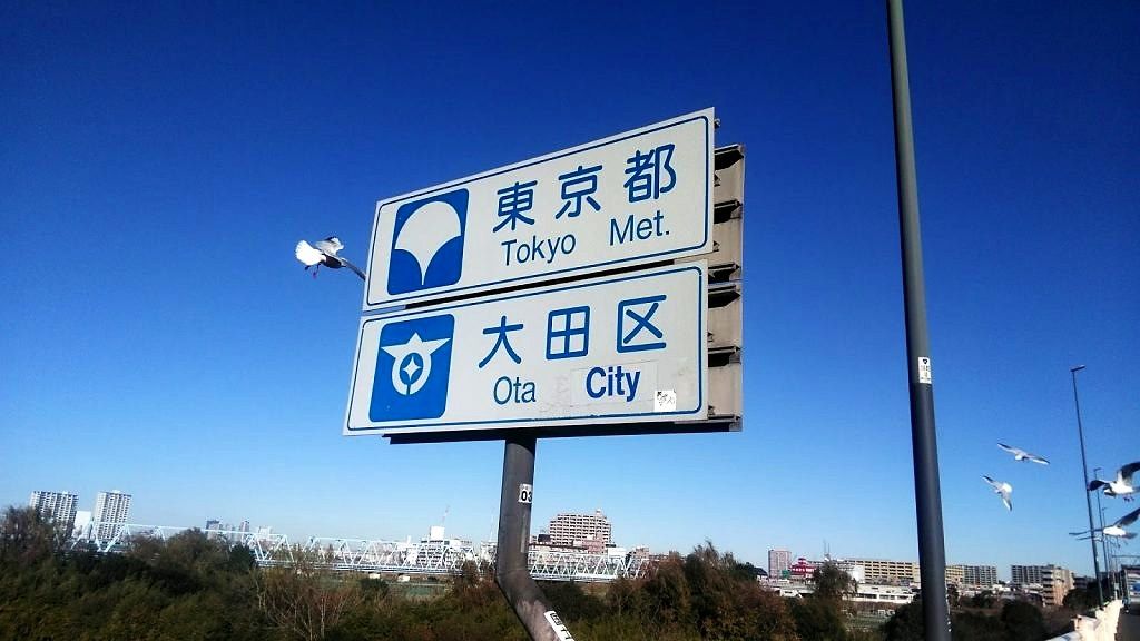 多摩川を渡った先の東京都大田区の標識。空にカモメが飛んでいる。