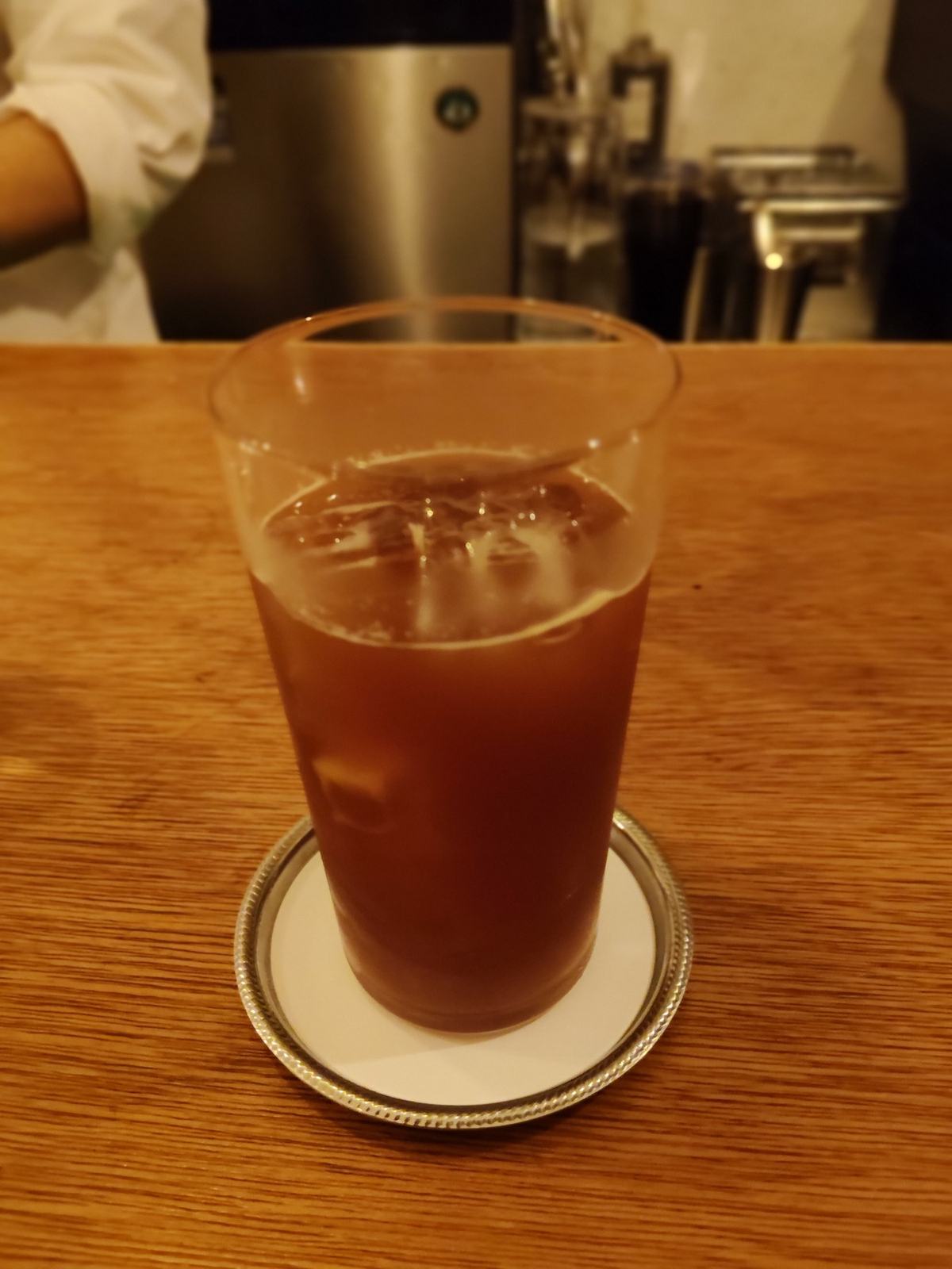 アイスアメリカーノ。銀の受け皿にのった背の高いグラスに、氷と琥珀色のコーヒー。