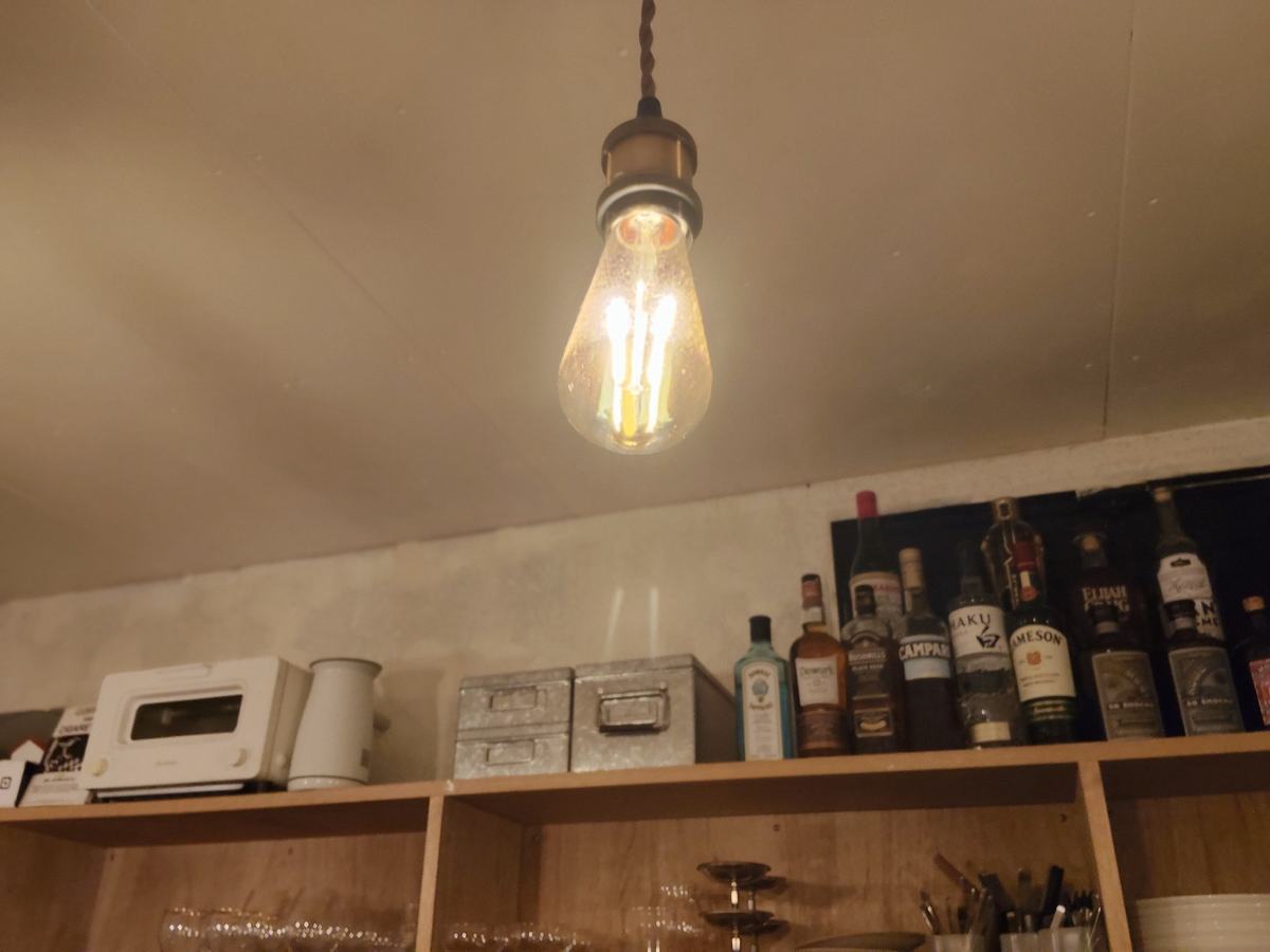 天井から吊るしたフィラメントの見える電球。下の棚には酒のボトルと小さなオーブントースター。