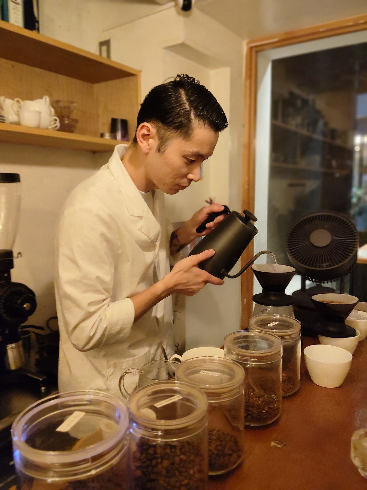 スタッフのたくみさんが黒いケトルからドリッパーへ湯を注ぐハンドドリップ。手前のカウンターに豆の瓶が並ぶ。