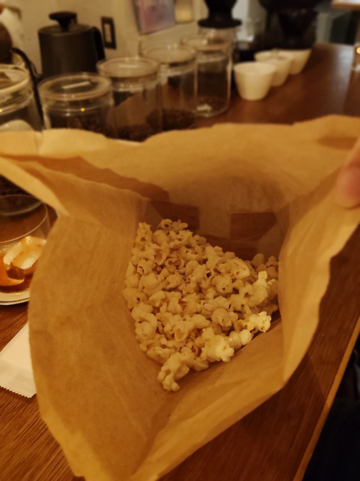 口を開いた紙袋の中のトリュフポップコーン。カウンターの奥に豆の瓶と白い器。