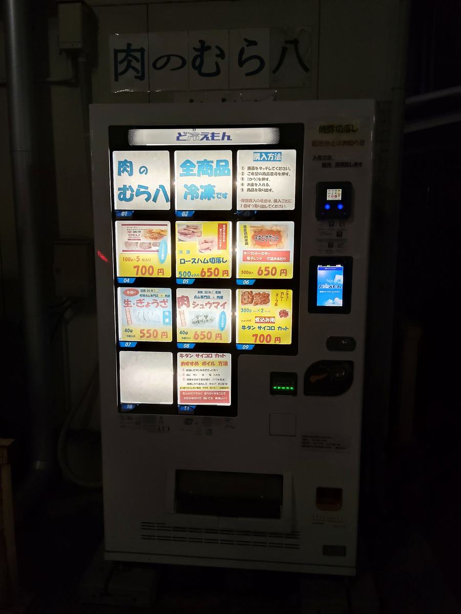 「肉のむら八」の冷凍肉の自販機。深夜の路上でライトに照らされている。