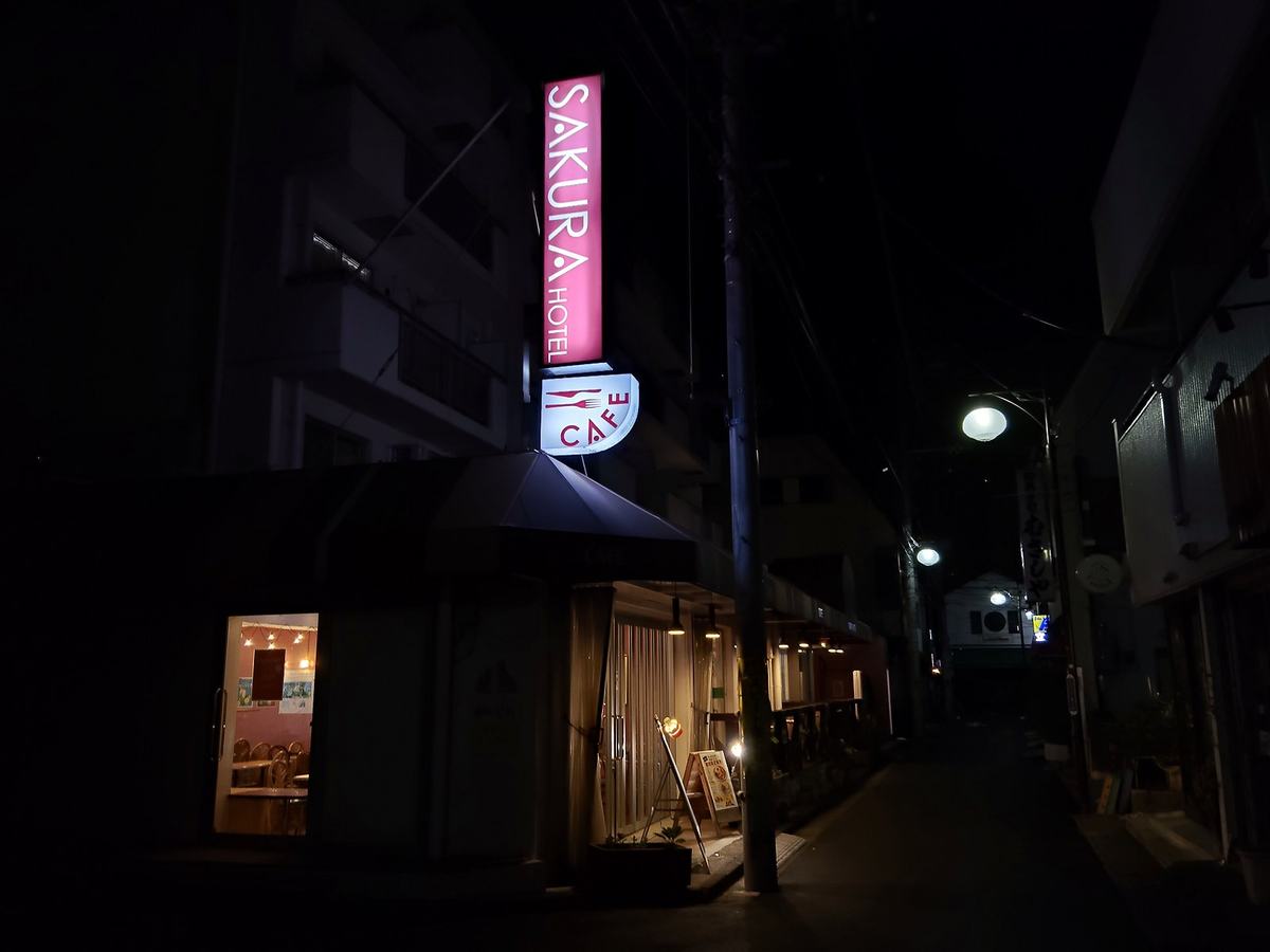 暗い路地に浮かぶ、サクラホテル日暮里のピンクの看板。
