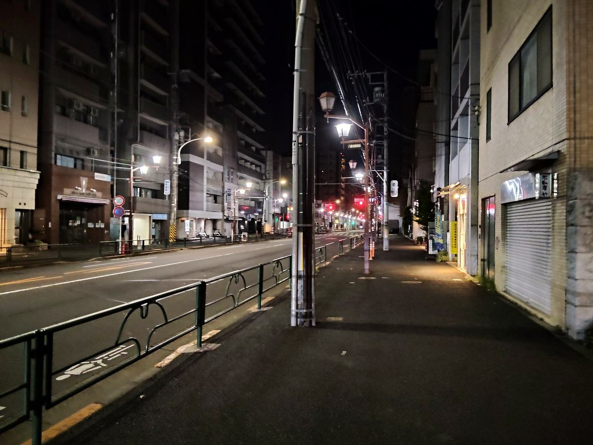 深夜の大通り沿いの歩道。街灯が並ぶだけで、前にも後ろにも人がいない。