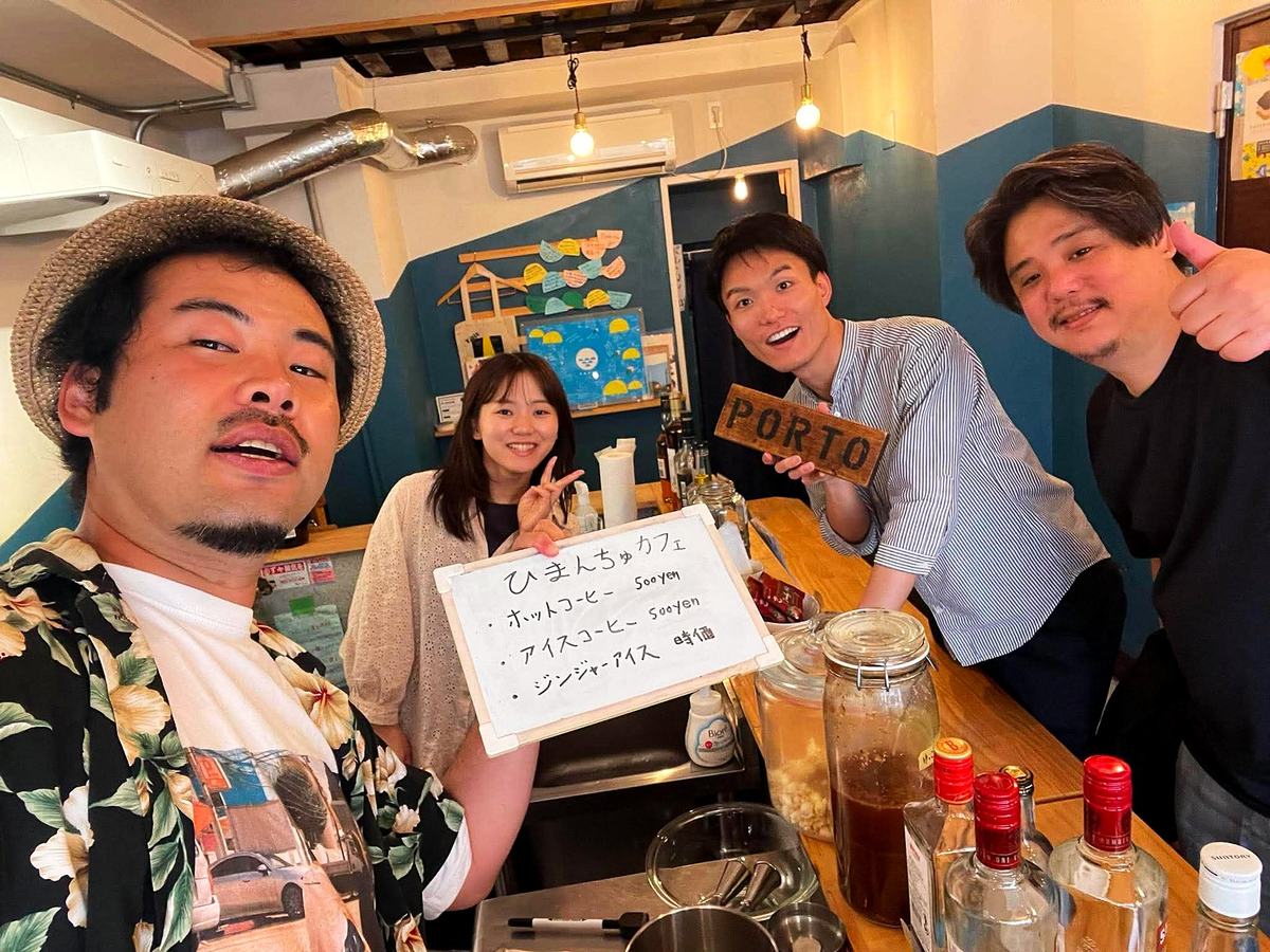 昼のPORTOカウンター。「ひまんちゅカフェ」と書かれたホワイトボードを囲む四人。