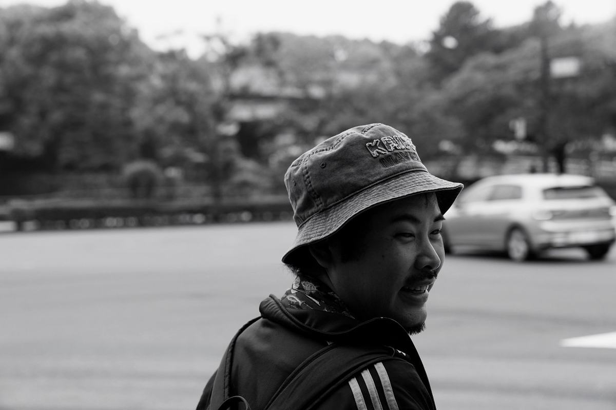 バケットハットをかぶって振り返り、笑う喜屋武さんのモノクロ写真。