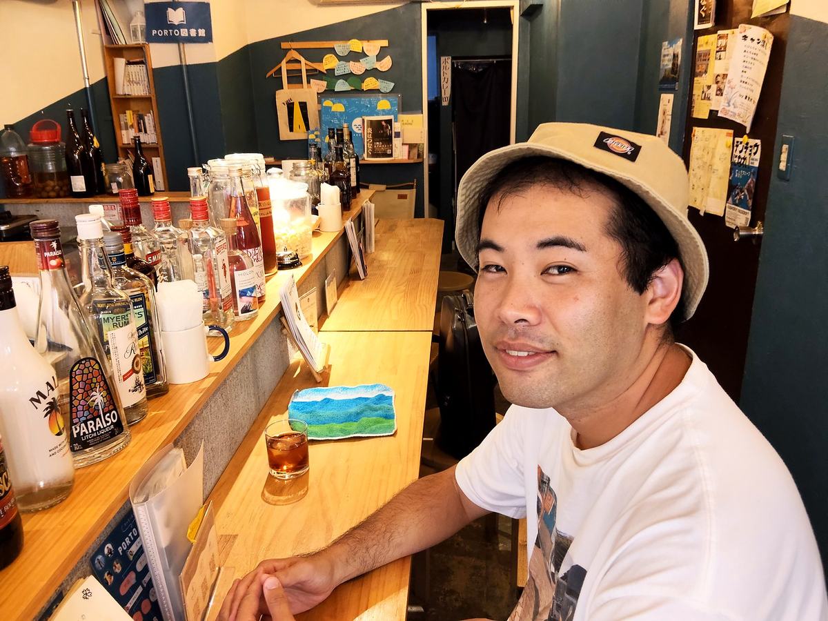 カウンター席に座って微笑む喜屋武さん。目の前にはグラス。