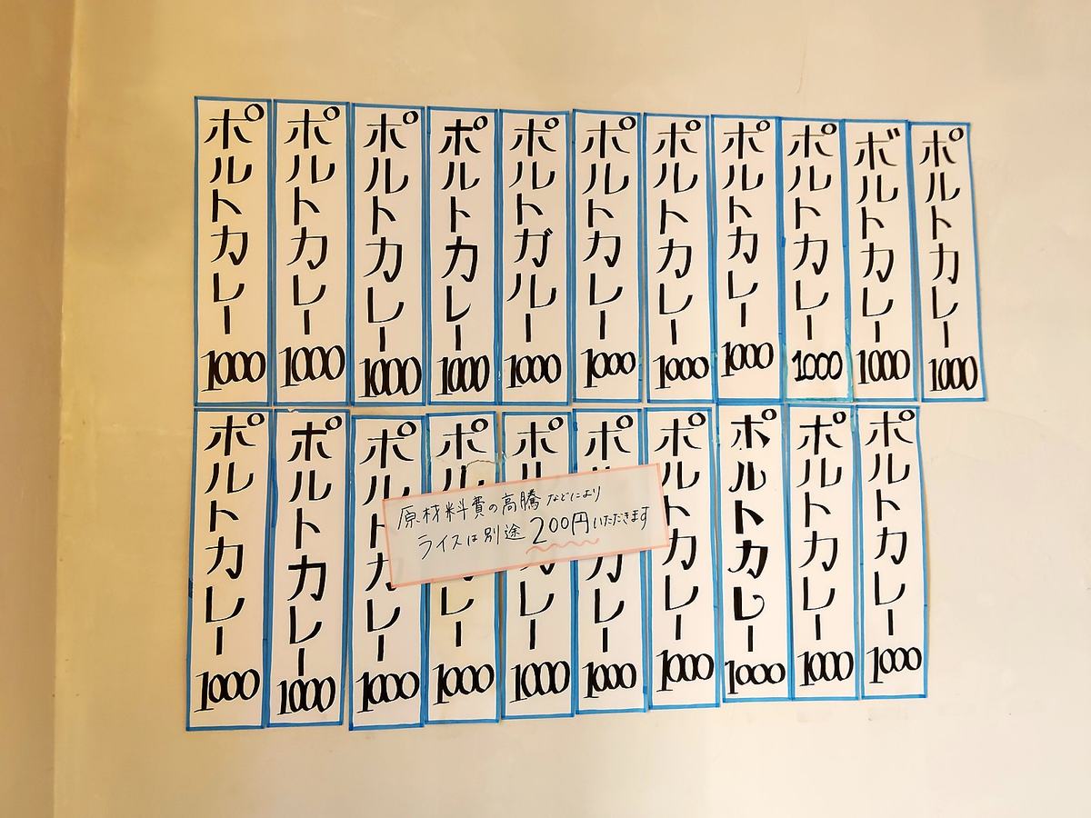 白い壁に貼られた二十数枚の手書き短冊。ほぼすべて「ポルトカレー1000」。中央にライス別途200円の注意書き。