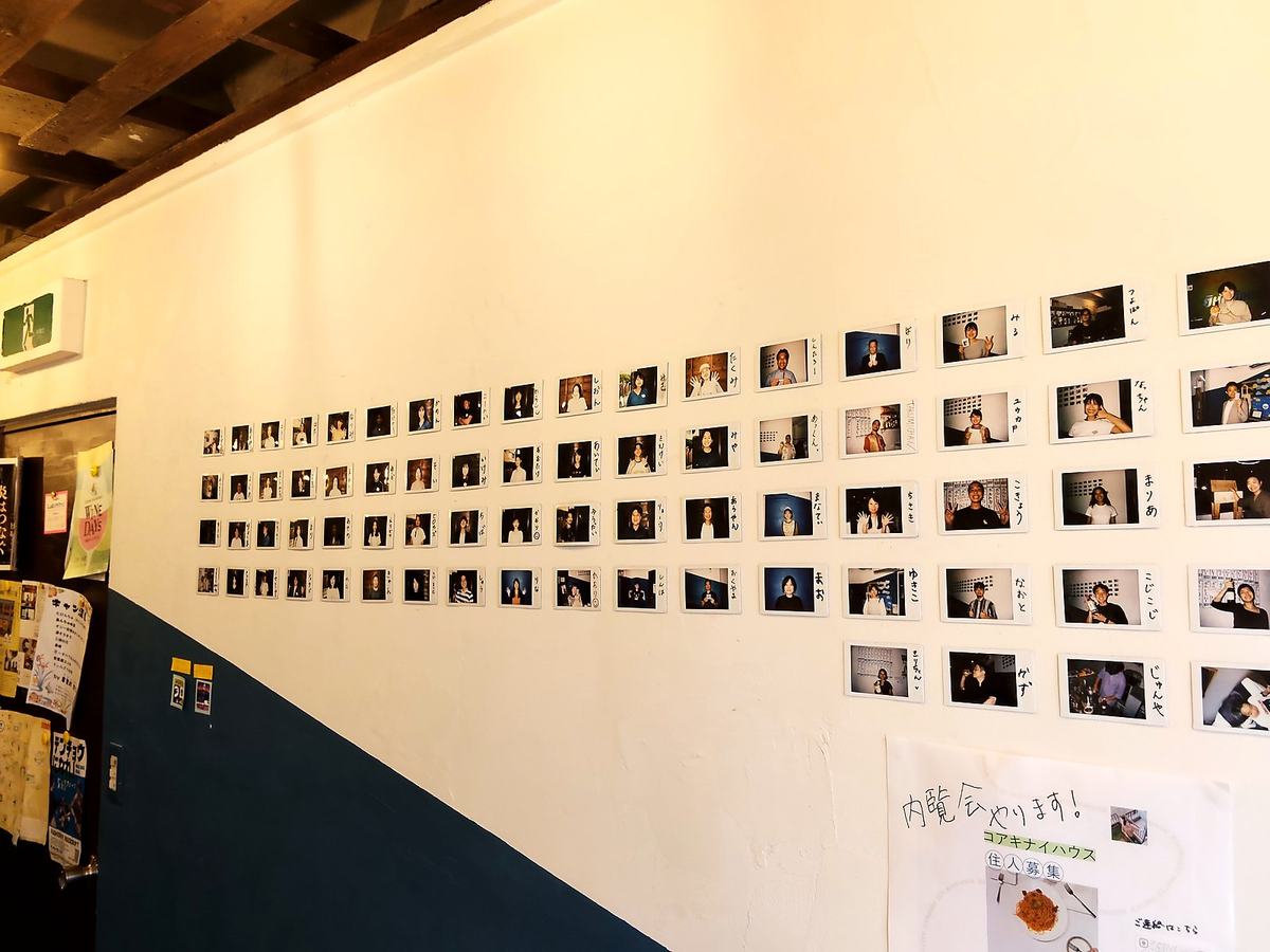 白い壁一面に貼られた、歴代の一日店長たちのチェキ写真。それぞれに手書きの名前が添えられている。