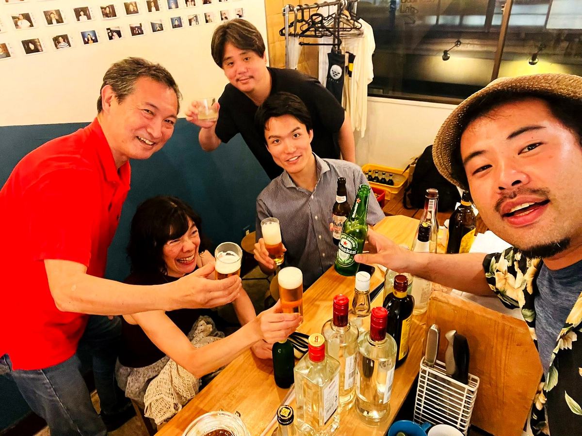 カウンターを囲んで五人がビールとグラスを掲げる乾杯。