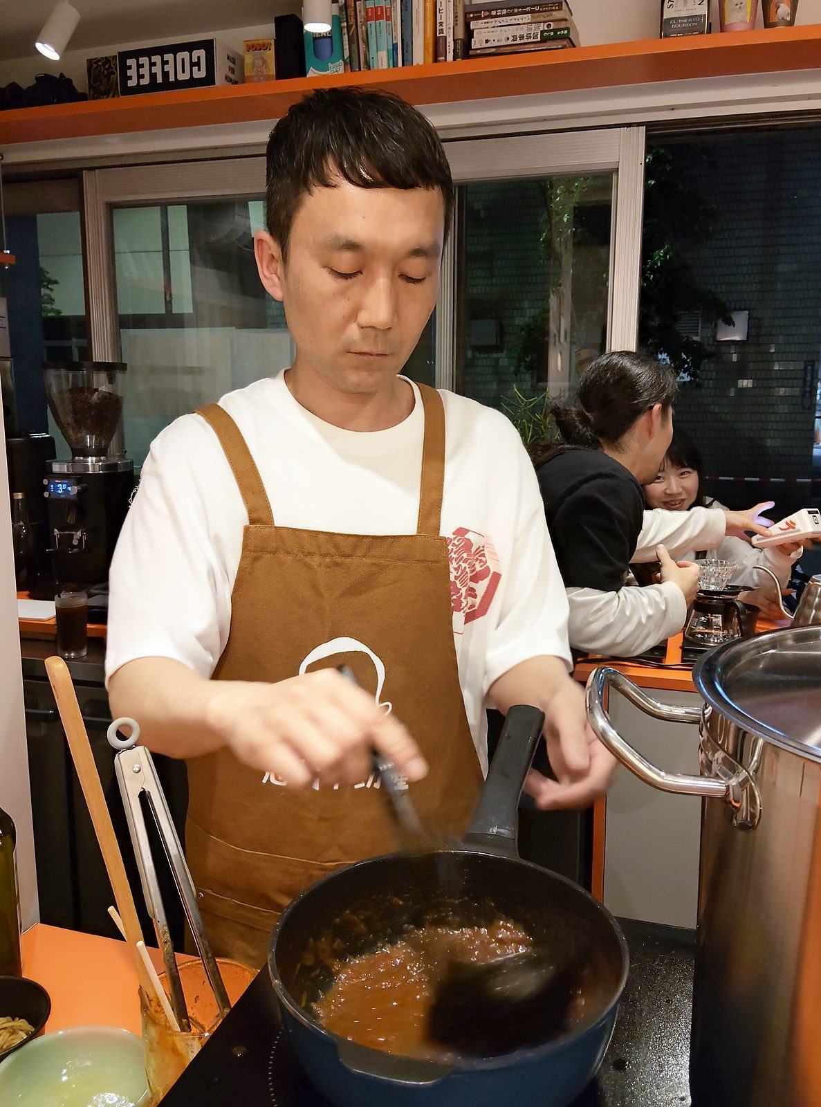 エプロン姿でシチューの鍋をふるうシムラさん。