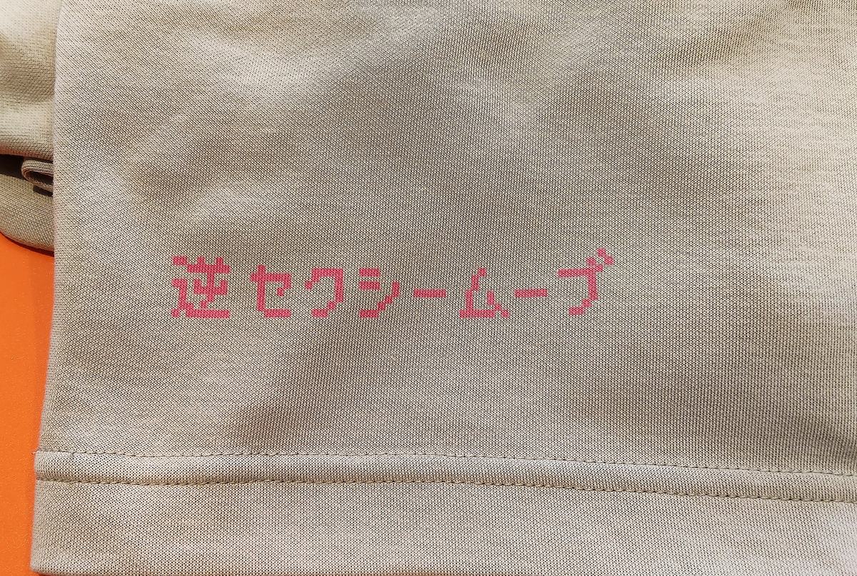 ベージュのTシャツの裾に、ピンクのドット文字で「逆セクシームーブ」とプリントされている。