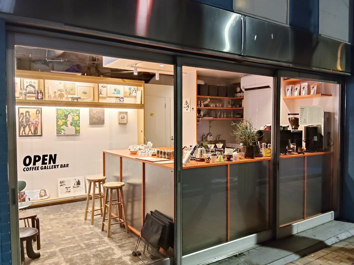 夜のテの店先。ガラス越しに明るいカウンターとスツールが見え、「OPEN COFFEE GALLERY BAR」の文字が出ている。