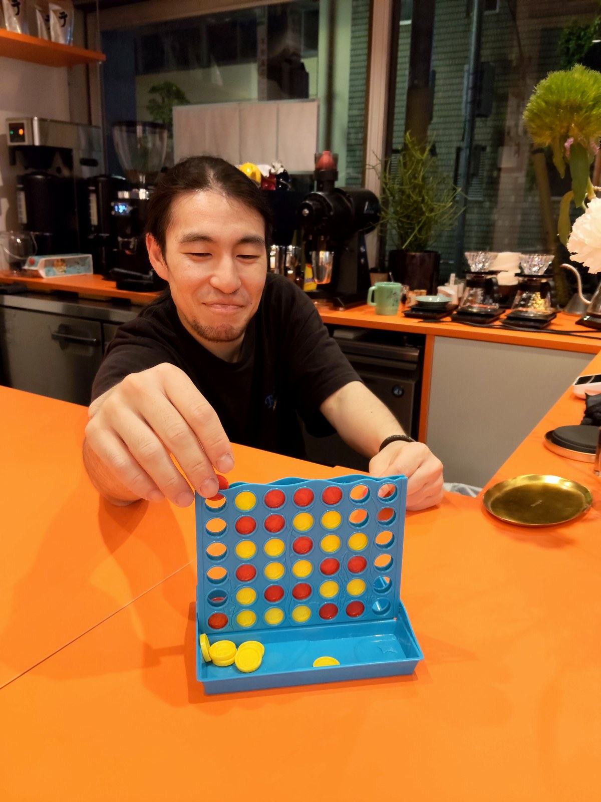 オレンジのカウンターで四目並べの駒を落とすテツさん。少し得意げな笑顔。