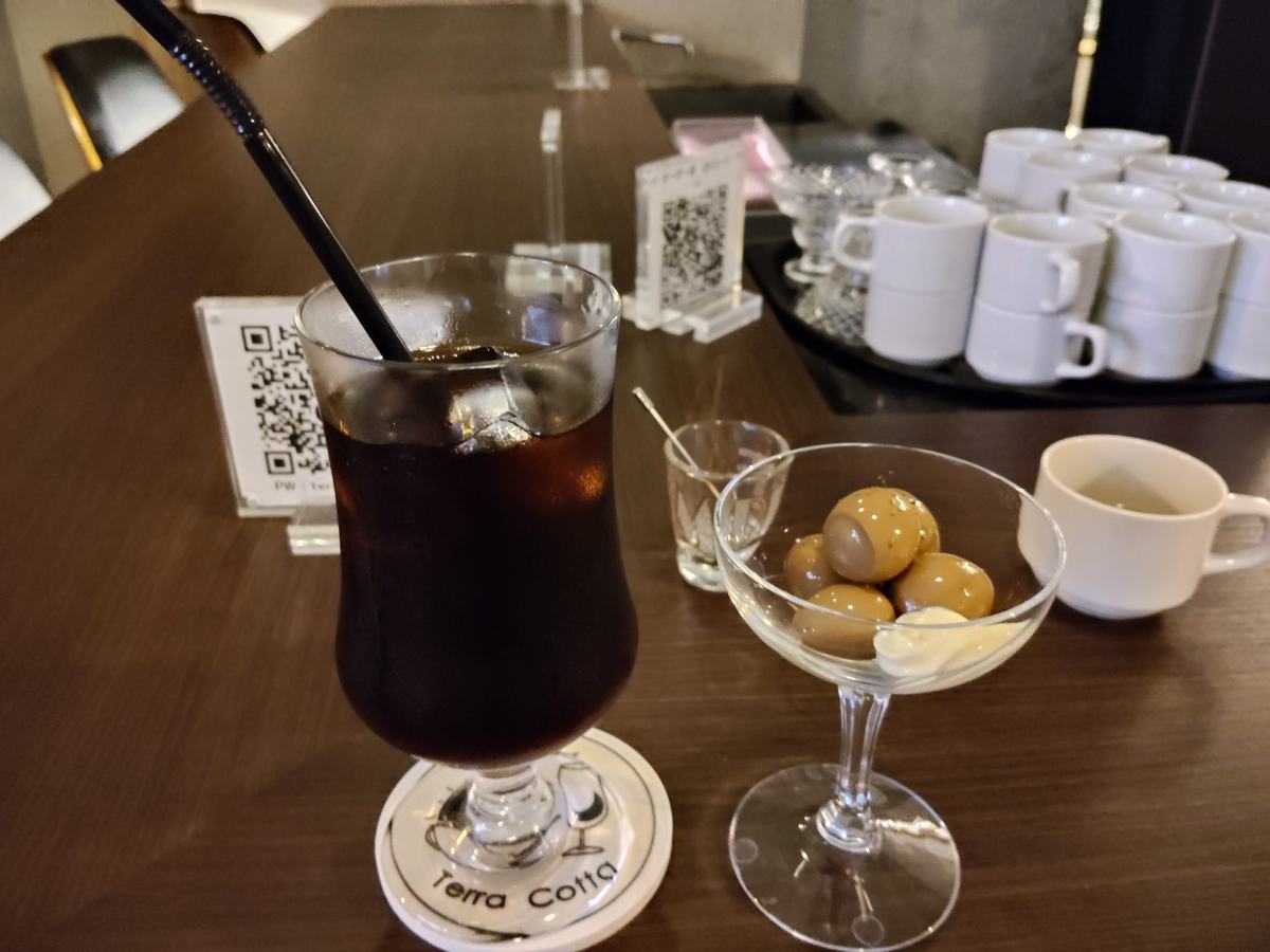 カウンターの上のアイスコーヒーと、ガラスの器に盛られた燻製の鶉の卵。マヨネーズが添えてある。グラスの下には店のコースター。