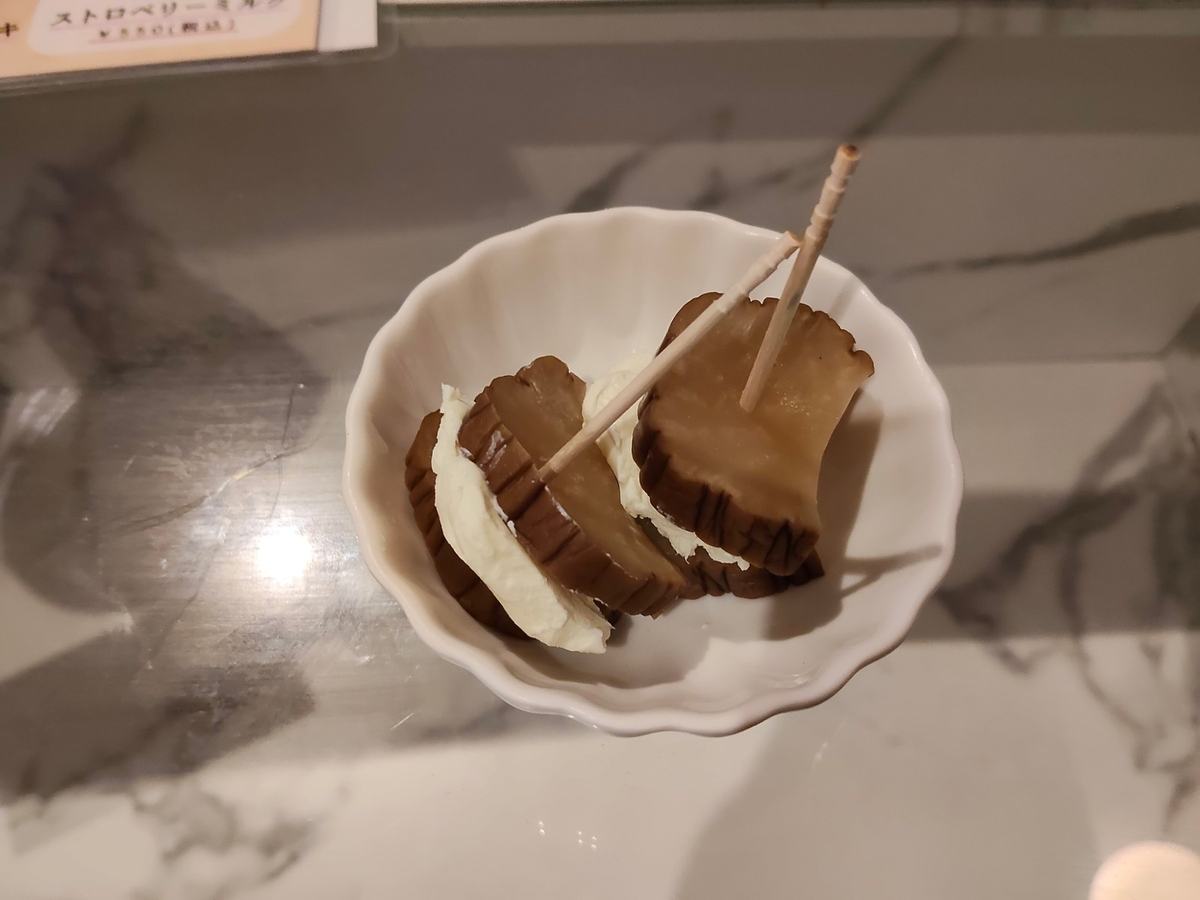 白い小皿に、いぶりがっこでクリームチーズを挟んだものが二切れ。爪楊枝が刺してある。