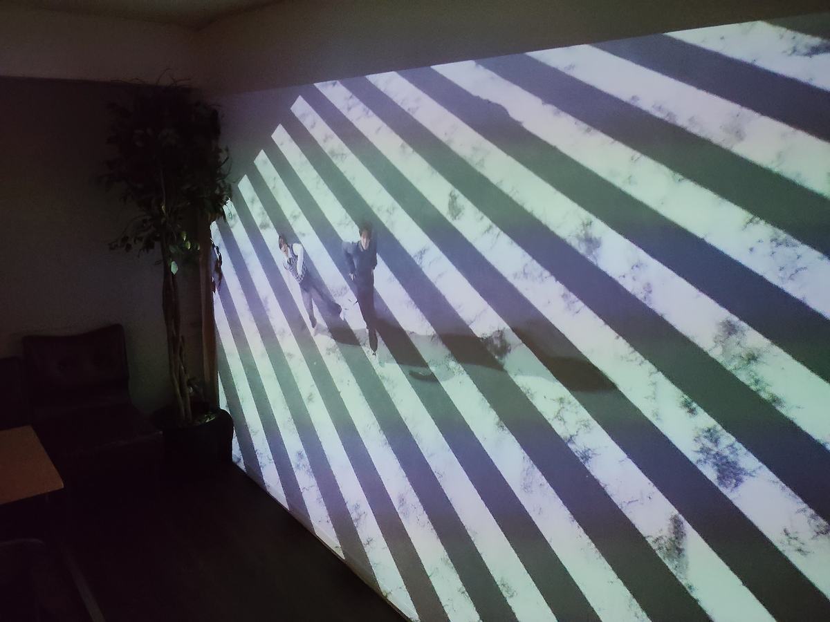 奥の壁一面に映し出されたプロジェクターの映像。手前にはテーブル席が並ぶ。