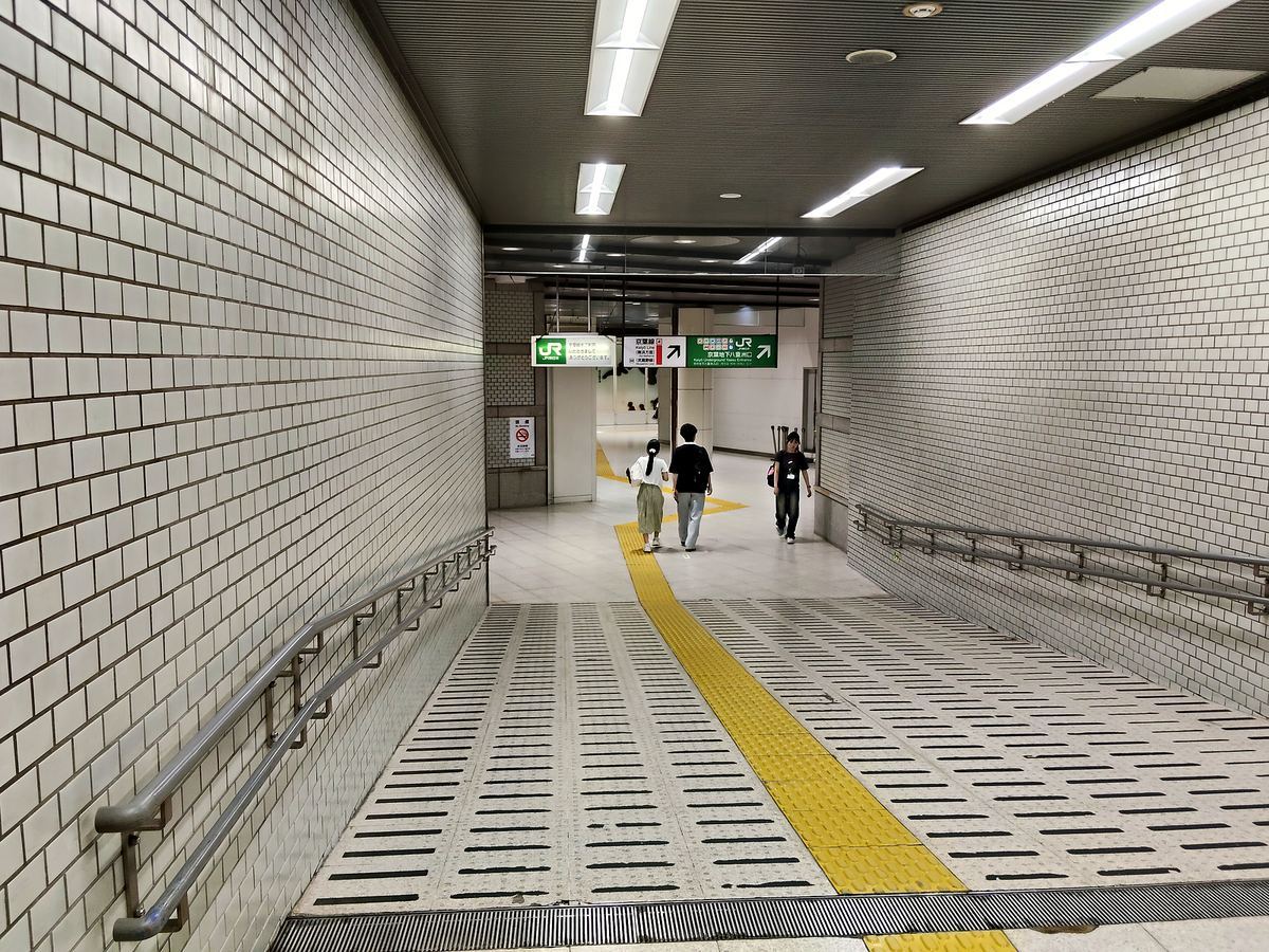 東京駅の京葉線沿いの長い地下通路。白いタイル張りで、床に黄色い点字ブロックが続いている。