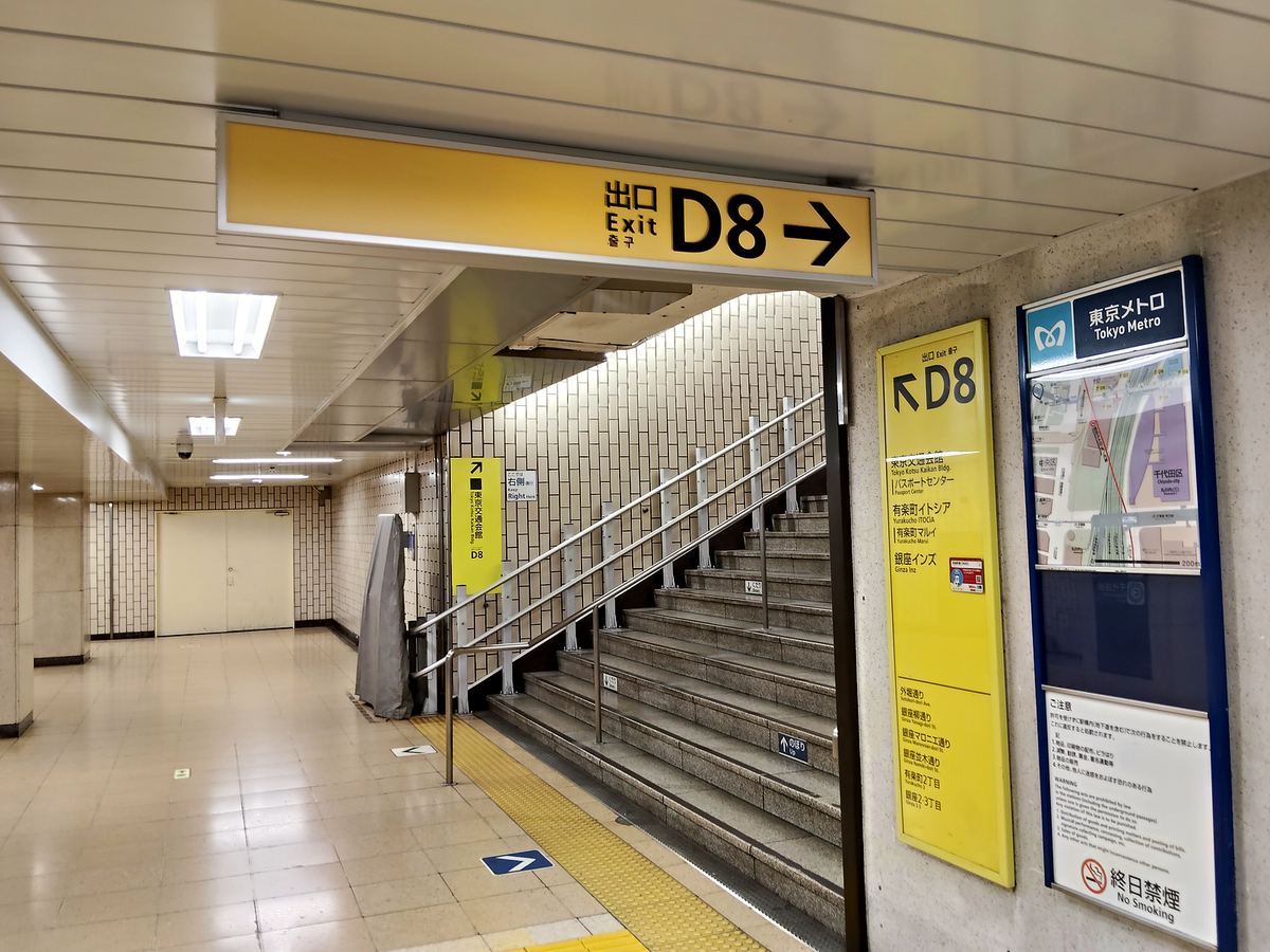 出口D8の階段。黄色い案内サインの下に、上りの階段と手すりが続いている。