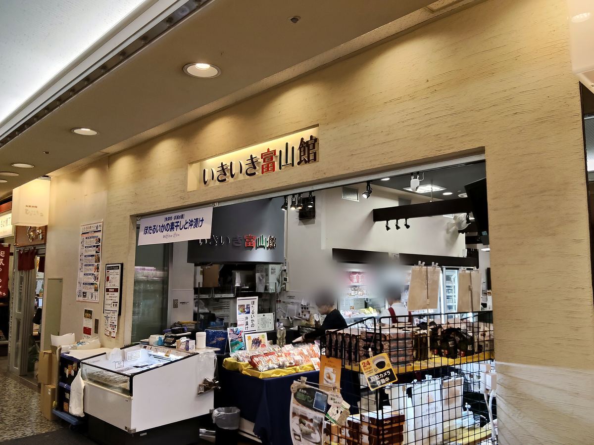 いきいき富山館の店先。ほたるいかの一夜干しの垂れ幕が下がり、冷蔵ケースが並んでいる。