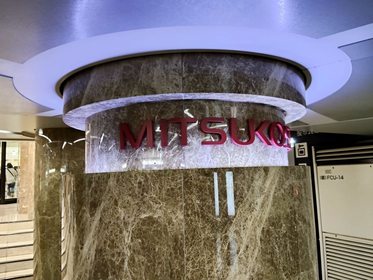 銀座三越の地下入口。大理石の柱の上に、赤い MITSUKOSHI のサインが光っている。