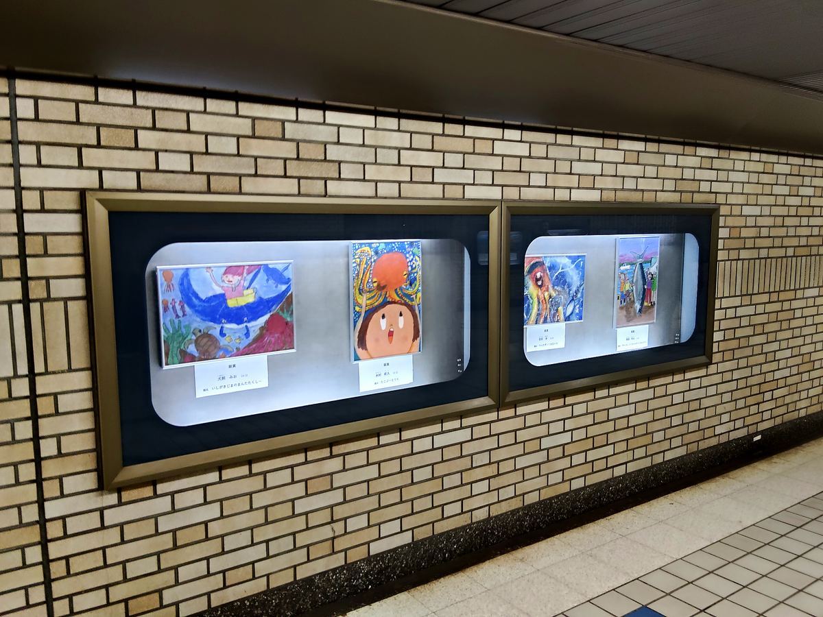 地下通路の壁の展示ケース。子どもの描いた絵が三点並んでいる。