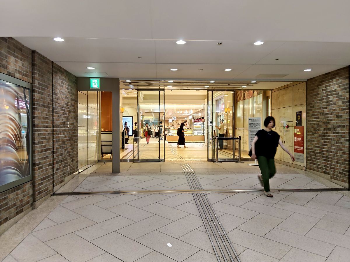 丸ビルの地下フロア。ガラスの自動扉の向こうに明るい店舗が並んでいる。